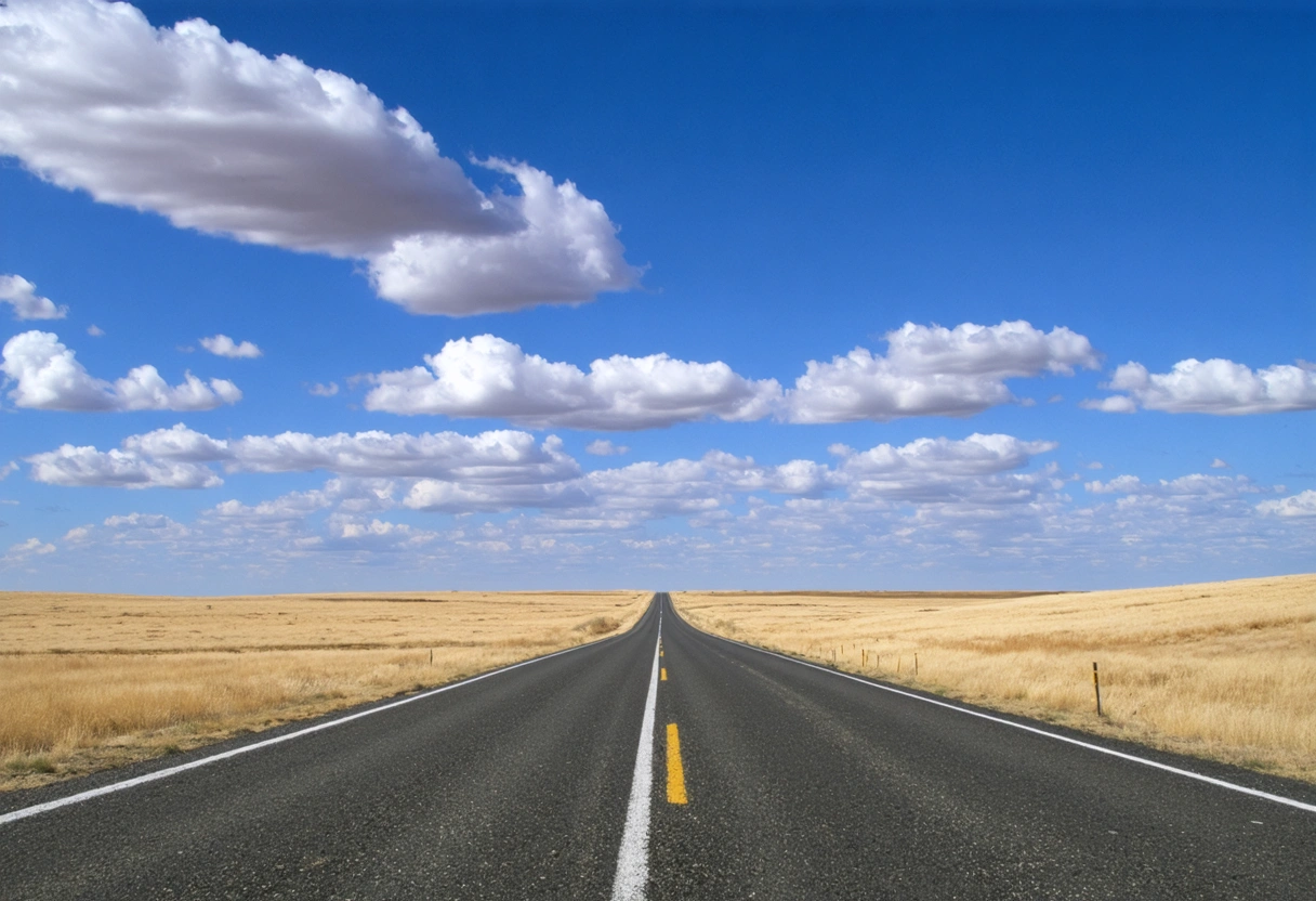 A two-lane highway stretching to the horizon through flat Prairie landscape under a wide blue sky